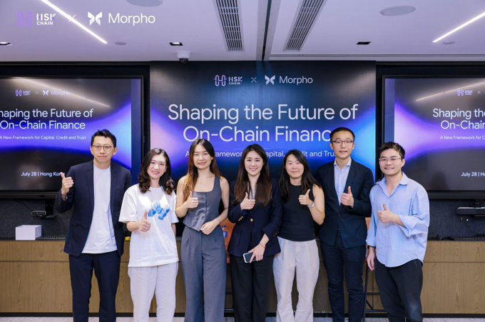 A group photo of seven professionals posing in front of displays reading "Shaping the Future of On-Chain Finance" alongside the HSK Chain and Morpho logos, dated July 28 in Hong Kong.