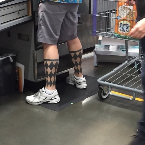 A person at a checkout area wears gray shorts and white sneakers with distinctive black and beige argyle-patterned knee-high socks, standing near a shopping cart.