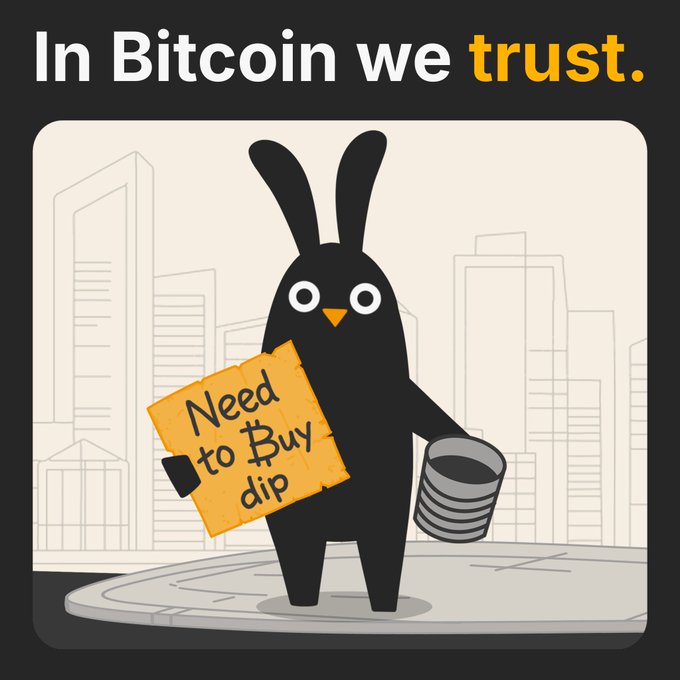 The image features a cartoon rabbit holding up a sign that says "Need to Buy Dip" while standing on a street corner with buildings in the background. The text above the rabbit reads "In Bitcoin we trust." This suggests that the rabbit might be promoting Bitcoin or cryptocurrency, possibly as part of an advertisement campaign for Bitcoin exchanges or ICOs (Initial Coin Offerings).