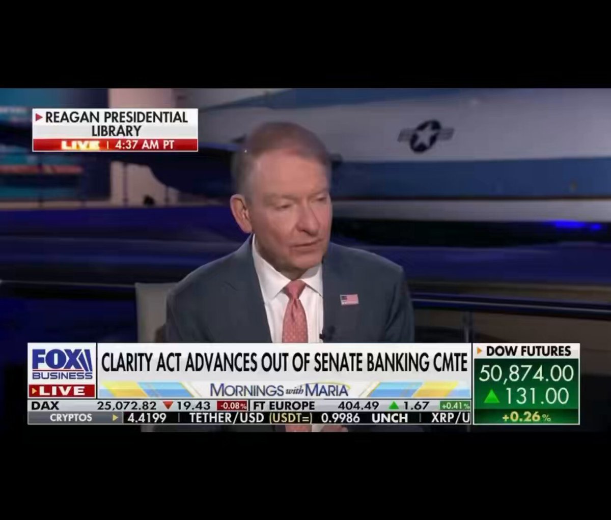 The image shows a man sitting at a desk, wearing a suit and tie, with his head resting on his hand as he looks down. The news program is playing on a television screen behind him, displaying the text "Focus on what is in the image and how it relates to the post". This suggests that the content of the image might be related to the discussion or topic being covered by the news program.