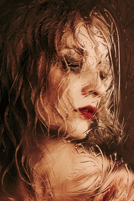 An artistic, painterly portrait of a woman with flowing, wind-swept hair rendered in warm brown, bronze, and red tones with a dreamy, ethereal quality.