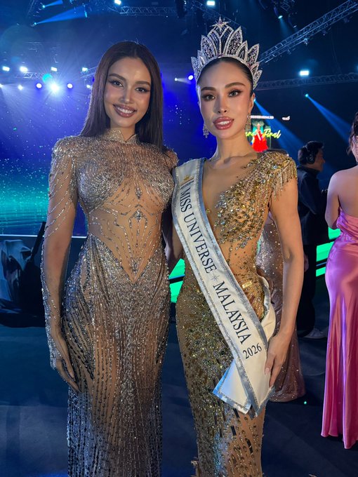 Two women pose together at a glitzy pageant event, with the woman on the right wearing a "Miss Universe Malaysia 2026" sash and an ornate crown while both don shimmering beaded evening gowns. The image illustrates the post's message, showing the same woman transitioning from her "crypto girl" appearance to her newly crowned Miss Malaysia title.