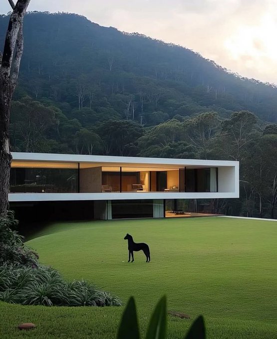 The image features a large white house situated at the bottom of a mountain with trees surrounding it. A black horse statue stands alone in front of the house, creating an interesting contrast between the man-made structure and the natural landscape. The scene is set against a cloudy sky, adding to the overall atmosphere of the image.