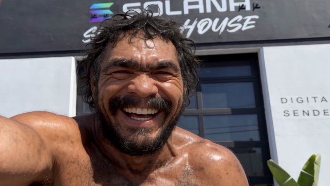 A shirtless, sweaty man with a beard takes a selfie outside a building labeled 'SOLANA BEACH HOUSE' with 'DIGITAL SEND' visible on the wall.