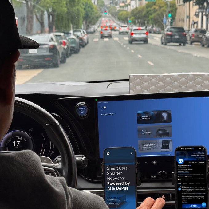 A view from the driver's seat of a vehicle showing a digital dashboard with a screen labeled 'assistant' featuring Mobile Assistant, Car Assistant, and Home Control Assistant, while a hand holds a phone displaying 'Smart Cars, Smarter Networks Powered by AI & DePIN'.