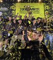 A team of cyclists in yellow and black jerseys celebrates under a shower of confetti, holding up a yellow "Jumbo-Visma" team banner and a bouquet of flowers, marking a victorious moment that reflects the post's bullish sentiment toward action sports.