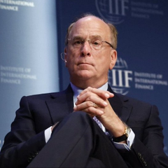A man in a dark suit, glasses, and blue tie sits with hands clasped, appearing to speak on a panel at an Institute of International Finance (IIF) event.