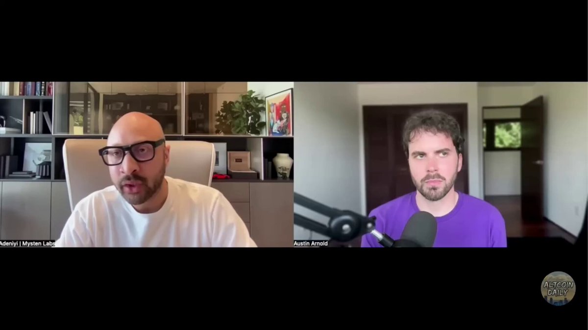 The image shows two men talking into a microphone, with one man wearing glasses and the other wearing a purple shirt. The background features a bookshelf filled with various items such as vases and potted plants. The caption of the image reads "Focus on what is in the image and how it relates to the post."