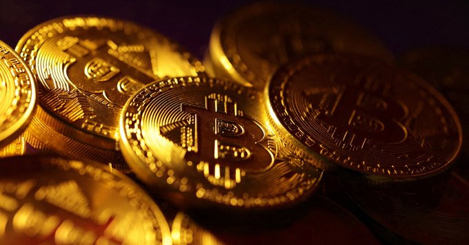 Several physical Bitcoin tokens with the iconic 'B' symbol are stacked together, illuminated by warm golden light.