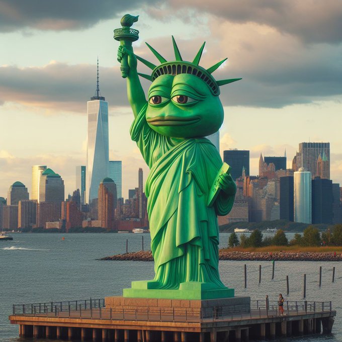 A whimsical green Statue of Liberty with a Pepe the Frog face stands on a pier with the New York City skyline, including One World Trade Center, in the background.