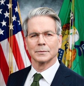 An official portrait shows a gray-haired man in a dark suit and green tie, with the American flag and a green flag visible in the background.