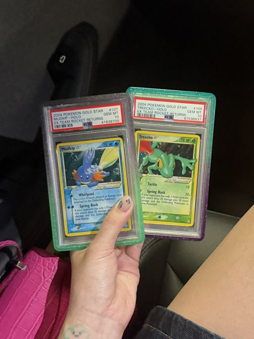 A hand holds two graded PSA 10 Pokémon cards—a 2004 Mudkip Gold Star Holo (#177) and a 2004 Treecko Gold Star Holo (#108), both from EX Team Rocket Returns—while the caption humorously suggests her husband is listing them for sale before they "moon," referencing crypto/stock market slang for a huge price spike. The image directly shows the valuable collectibles being discussed for potential sale.