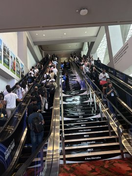 A photograph showing a crowded pair of escalators in a shopping mall or transit station, with many people riding up and down the steps.