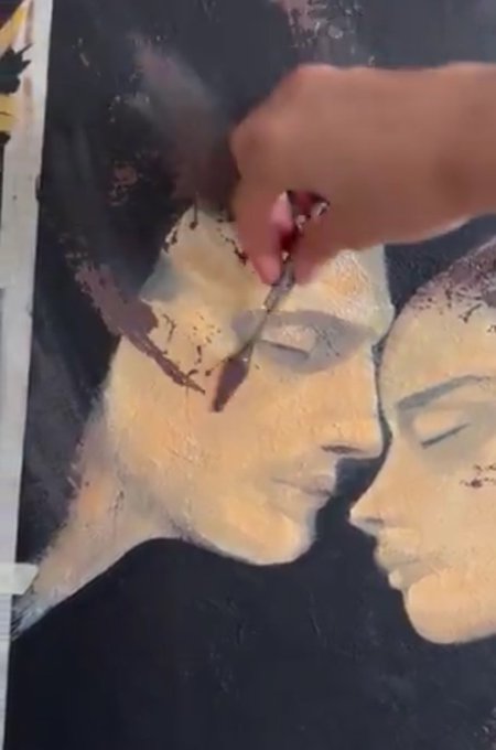 A close-up of a person's hand painting a portrait of two faces on a canvas, focusing on the eye area.