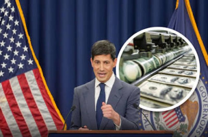 A man in a gray suit speaks at a podium flanked by the American flag and a Governor's flag, with an inset image of currency being printed on a press.