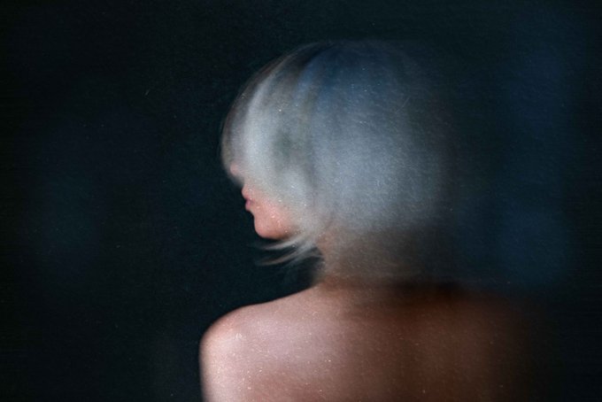 A blurry profile portrait of a woman with pale blonde hair against a dark, moody background, evoking a dreamlike, ethereal aesthetic that aligns with contemporary fine art photography featured on "ART ON ETH." The intimate framing and soft focus create a haunting, artistic mood fitting for an Ethereum-based art collection.