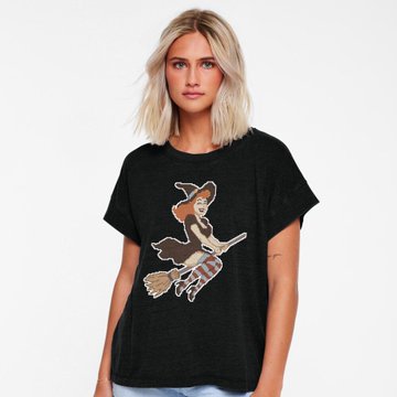 A product photo of a blonde woman modeling a black t-shirt featuring a cartoon witch on a broomstick design.
