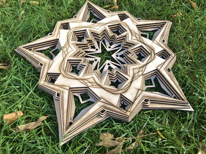 An intricate laser-cut wooden star ornament with layered geometric patterns rests on green grass.
