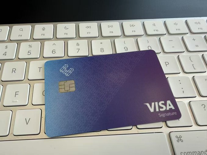 A purple and blue gradient Visa Signature credit card featuring a chip and EMV symbol rests on the keys of a white Apple keyboard, with the Visa Signature logo visible in the bottom right corner.
