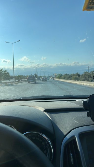 A view from inside a car driving on a highway under a clear blue sky, with a speedometer visible on the dashboard.