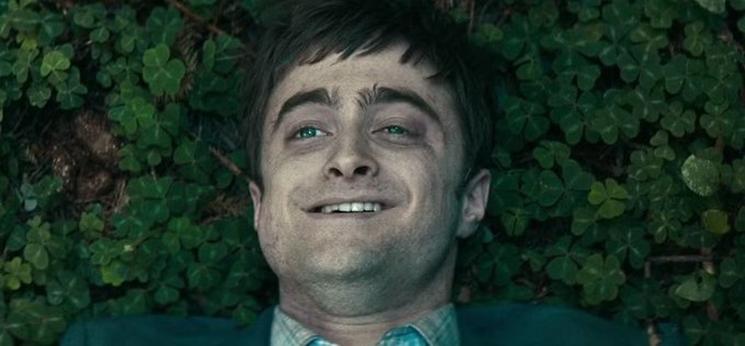 Actor Daniel Radcliffe lies among clover leaves, smiling up at the camera.