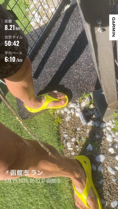 The image shows a person's feet wearing yellow flip flops, with their legs visible from behind them. The photo appears to be taken outdoors, possibly at a park or beach setting. The caption of the image includes Japanese text that reads "8キロ 台湾サンダル レースは台湾サンダルと決めたので早速練習 なんて軽いんだ！...ちゃっても楽チンごとによる". This text is likely a description of the person's footwear or an interesting detail about their surroundings.