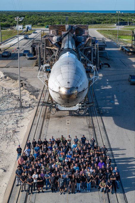 A large group poses for a team photo in front of a rocket fairing at a launch facility, likely SpaceX's Starbase, symbolizing additional launch capacity now available for AST SpaceMobile ($ASTS) satellite deployment.