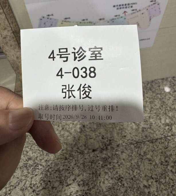 A hand holds a Chinese hospital queue ticket for "4号诊室" (Room 4) with ticket number 4-038 for a patient named "张俊" (Zhang Jun), taken at a medical institution with a floor plan visible in the background.

The image relates to the post by visually echoing the experience of "going crazy" under pressure—standing in line at a hospital waiting to see a doctor is a universally stressful, often maddening experience that parallels the exhausting grind of engaging with hundreds of posts daily on X.