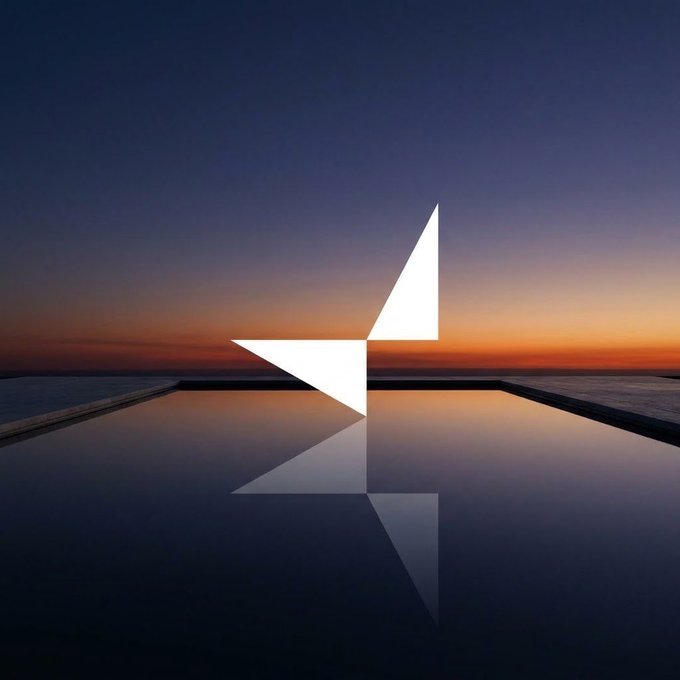 A minimalist landscape photograph at dusk showing a geometric light installation reflected in a still pool of water, set against a gradient sky transitioning from orange to deep blue.