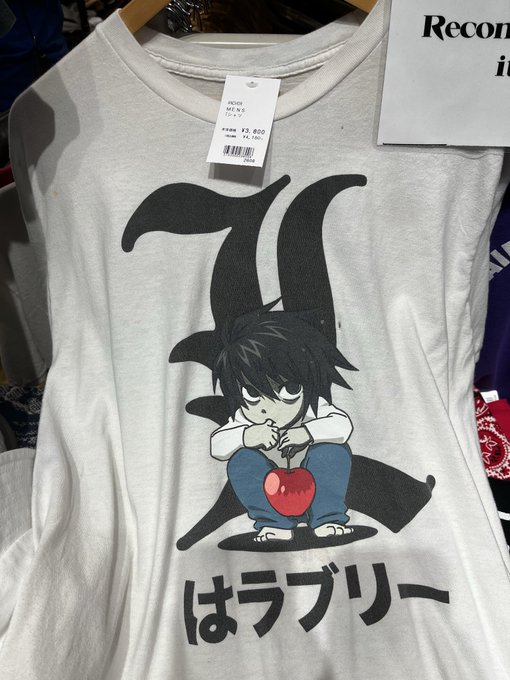 A gray t-shirt displayed on a hanger features a black kanji character with a small anime-style boy holding a red apple, and the Japanese text "はラブリー" (Hana Lovely) below, priced at ¥2,800. The cute, chibi-like design matches the "alacam gibi" (like a baby/innocent) comment, evoking a sweet and innocent aesthetic.