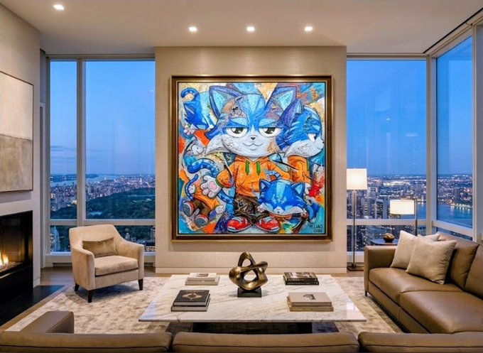 A vibrant, large-scale abstract painting of a blue cat character titled "The Centerpiece" dominates the wall of a luxurious high-rise living room, framed by floor-to-ceiling windows showcasing a sweeping city skyline at dusk. The colorful artwork, featuring $Toshi as the "Face of Base," serves as the room's bold focal point above a marble coffee table and elegant seating area, perfectly fitting its role as a centerpiece.