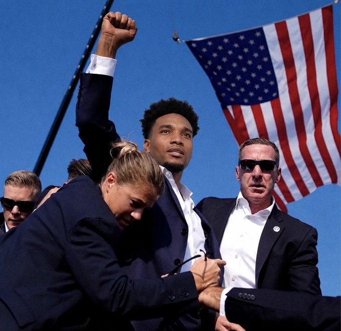 A man with his fist raised stands before the American flag, perhaps a symbolic representation of the ticker $ANSEM for president. The image evokes a sense of patriotism and a call to action.