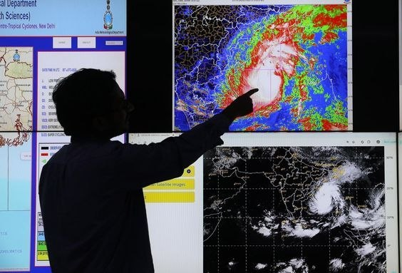A silhouetted man pointing at a large screen displaying weather radar/satellite imagery of a cyclone over a coastal region, with 'Earth Sciences' and 'Tropical Sciences, New Delhi' partially visible.