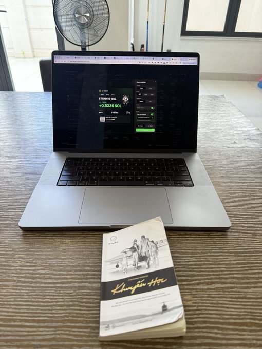 A MacBook laptop on a wooden desk displaying a crypto wallet showing 'ETHWB2-SOL +0.5235 SOL', with a 'Khumba' branded pamphlet placed in front of the laptop.