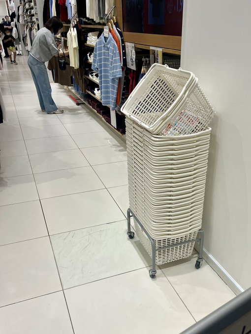 しますので, this image shows a person standing next to a stack of white baskets or laundry baskets that are lined up against a wall. The baskets appear to be empty at the moment but could potentially hold more items if needed.