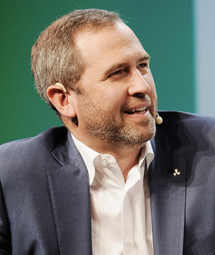 Brad Garlinghouse, CEO of Ripple, is shown speaking at an event, appearing engaged and smiling. His image accompanies news about Ripple's decision to fight rather than shut down after the SEC's 2020 lawsuit over XRP.