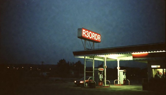 A nighttime photograph of a gas station with a bright red illuminated sign reading 'R3ORDR' against a dark blue sky.