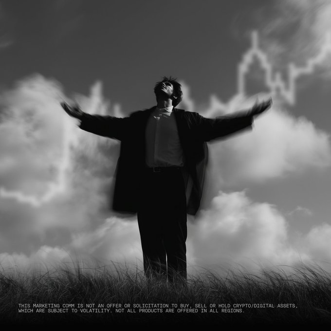 A black-and-white image shows a man in a suit standing in a grassy field with arms outstretched and head tilted back toward a cloudy sky overlaid with a faint city skyline, accompanied by the disclaimer: "THIS MARKETING COMM IS NOT AN OFFER OR SOLICITATION TO BUY, SELL OR HOLD CRYPTO/DIGITAL ASSETS, WHICH ARE SUBJECT TO VOLATILITY. NOT ALL PRODUCTS ARE OFFERED IN ALL REGIONS." The triumphant, skyline-reaching pose visually captures the optimistic "we're back" sentiment expressed in the post.