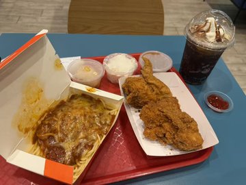 The image shows a dining table with two trays of food, including pasta dishes and fried chicken. The trays are placed next to each other, creating an appetizing display for potential diners. A drink can be seen on the side as well. The overall scene suggests that this could be a meal being served at a restaurant or a gathering where people have come together to enjoy food and drinks.