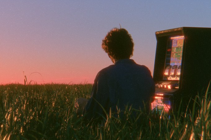 A person sits in a grass field at sunset, facing a glowing slot machine—a surreal, dreamlike scene fitting the context of selling an artwork to @tropical1ceberg for $606, with the imagery symbolizing the gamble and reward of the sale.