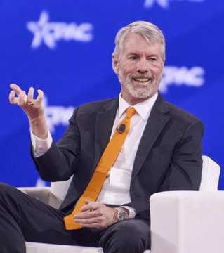 A man with a gray beard wearing a dark suit and orange tie gestures while speaking at a CPAC event.