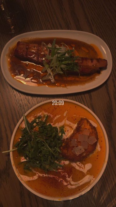 Two plates of food are displayed on a wooden table, one featuring salmon with shredded scallions in a brown sauce, and the other showing salmon with arugula in a creamy orange soup, with a timestamp of 20:09 visible.