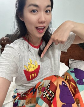 A woman wearing a grey McDonald's fries t-shirt points to the graphic on her shirt with a smile.