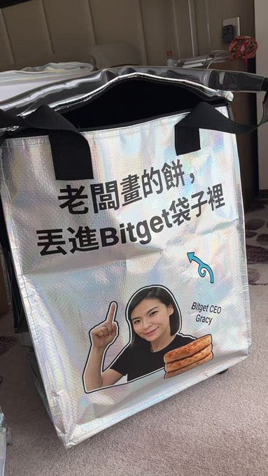 A silver insulated bag featuring Bitget CEO Gracy with Chinese text reading '老闆畫的餅，丟進Bitget袋子裡' (Throw the boss's pie into the Bitget bag), alongside an image of pastries.