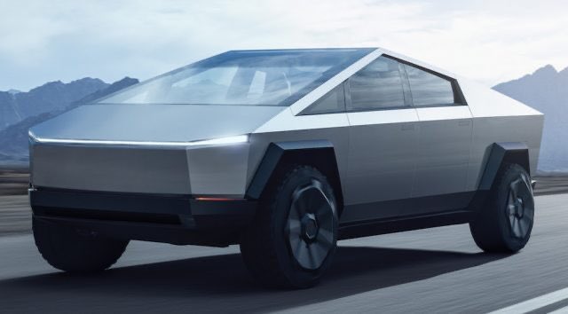A silver Tesla Cybertruck driving on a road with mountains visible in the background.