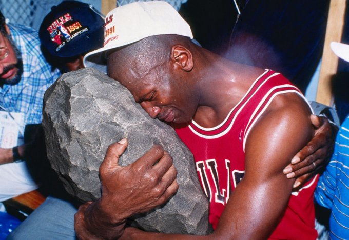 Michael Jordan crying while holding the 1996 Chicago Bulls NBA Championship trophy, wearing his iconic red Bulls jersey and a championship cap.