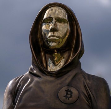 The image features a bronze statue of a person wearing a hooded sweatshirt, which appears to be a mask or a hoodie. The statue has a face that looks like a mask with a gold background, giving it an intriguing appearance. The caption below the statue reads "Satoshi Nakamoto disappeared forever: April 23, 2001 - sends a private email to Mike Hearn - one of the earliest Bitcoin developers - talks about time locks and OP codes - warns about risks with block reorganizations". This suggests that the image is related to the story behind the creation of Bitcoin.