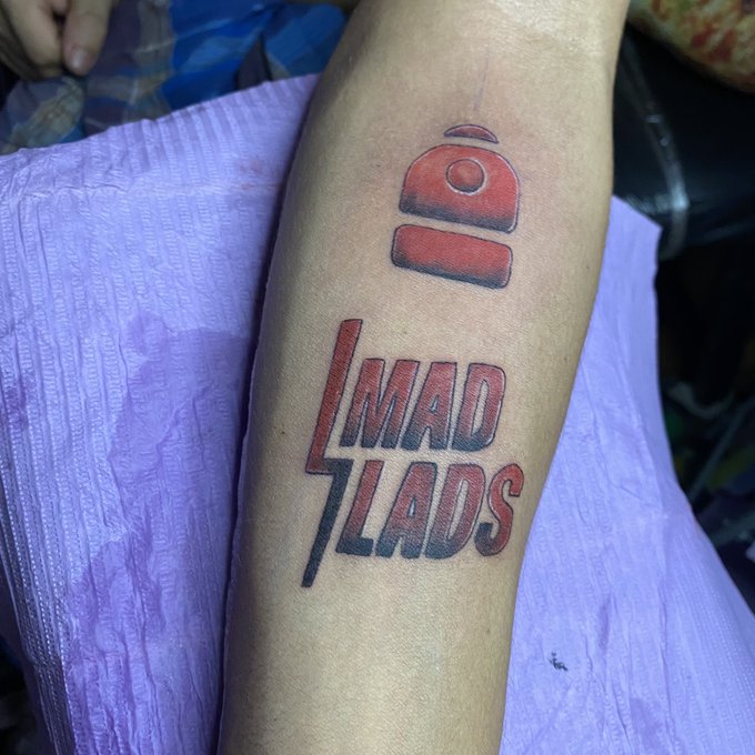 A fresh tattoo on someone's forearm featuring a red bell icon above the stylized text 'MAD LADS' in red and black lettering.