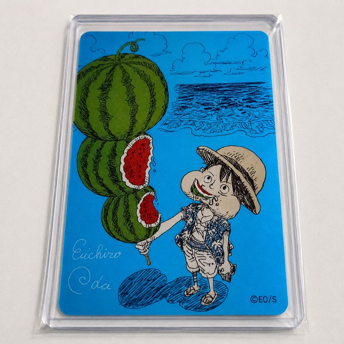 An illustrated card or sticker in a plastic sleeve showing a cartoon boy eating watermelon at the beach, signed 'Eiichiro Oda' with ©EO/S.