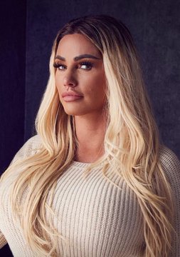 A portrait photo of a woman with long blonde hair wearing a white knit sweater, posing in front of a dark gradient background.